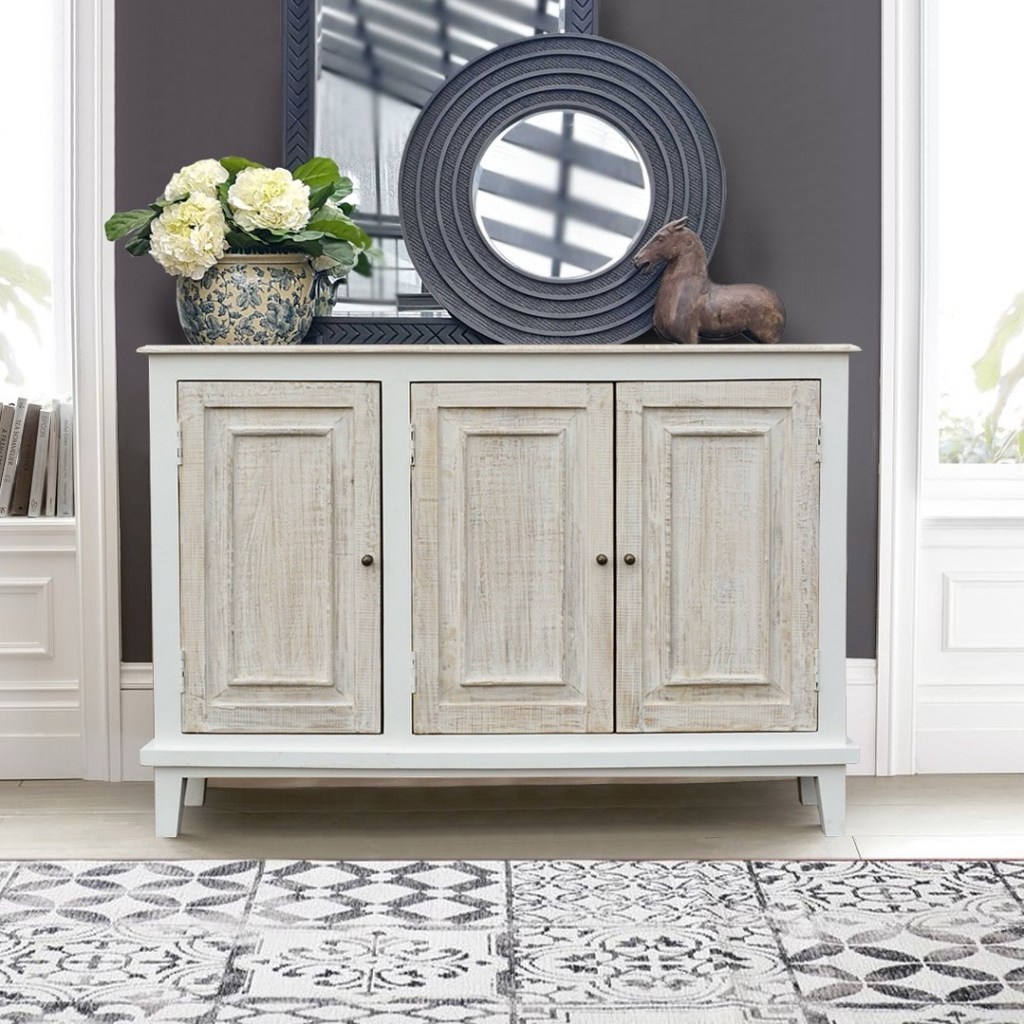 Płytka drewniana komoda Hampton Island w stylu vintage i boho, bielona, z trzema drzwiami, ustawiona we wnętrzu z lustrem i dekoracyjnymi dodatkami – Karina Meble Janki.