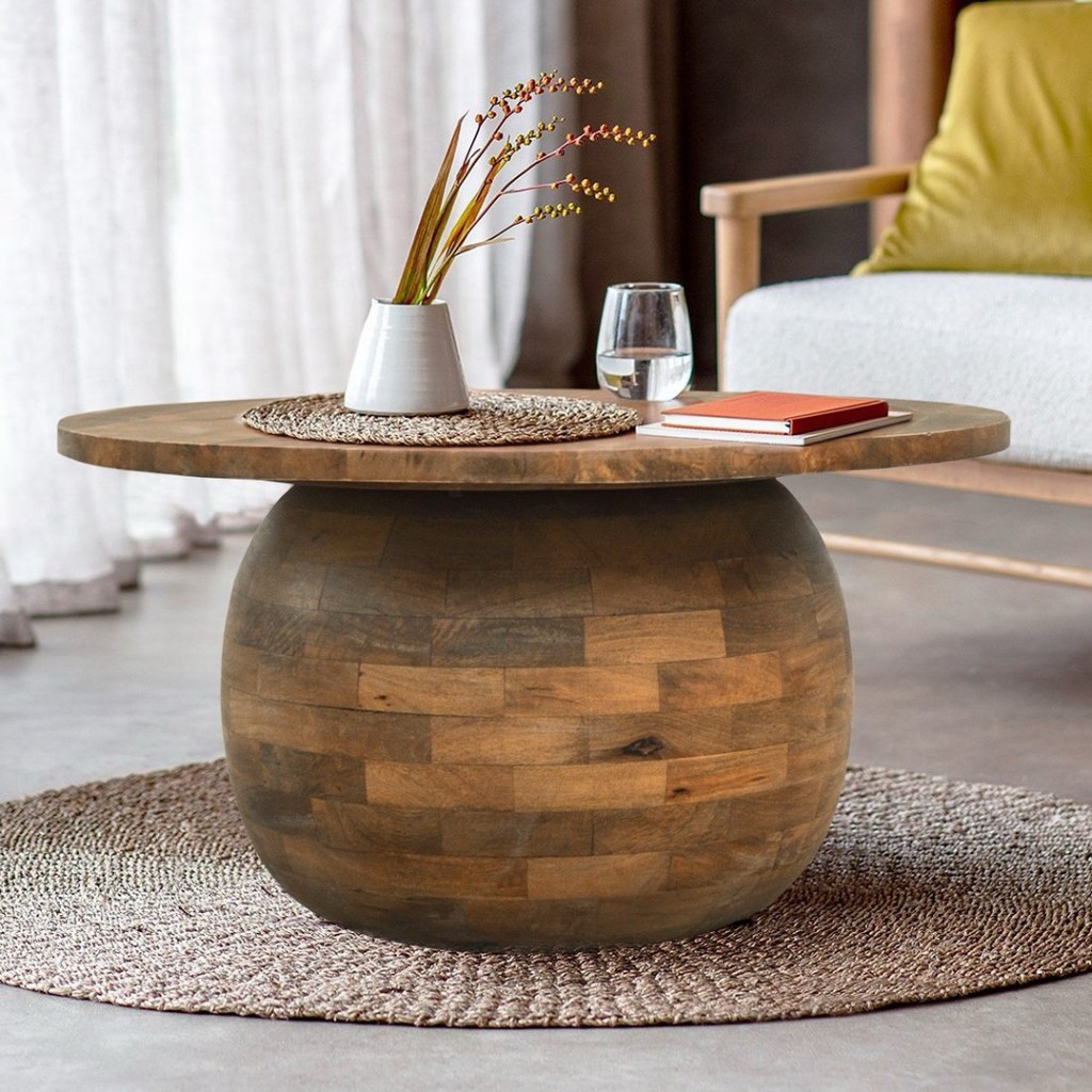 Okrągły stolik kawowy z litego drewna mango w stylu indyjskim, z patynowaną brązową powierzchnią i masywną, kulistą podstawą, ustawiony na plecionym dywanie w przytulnym wnętrzu.