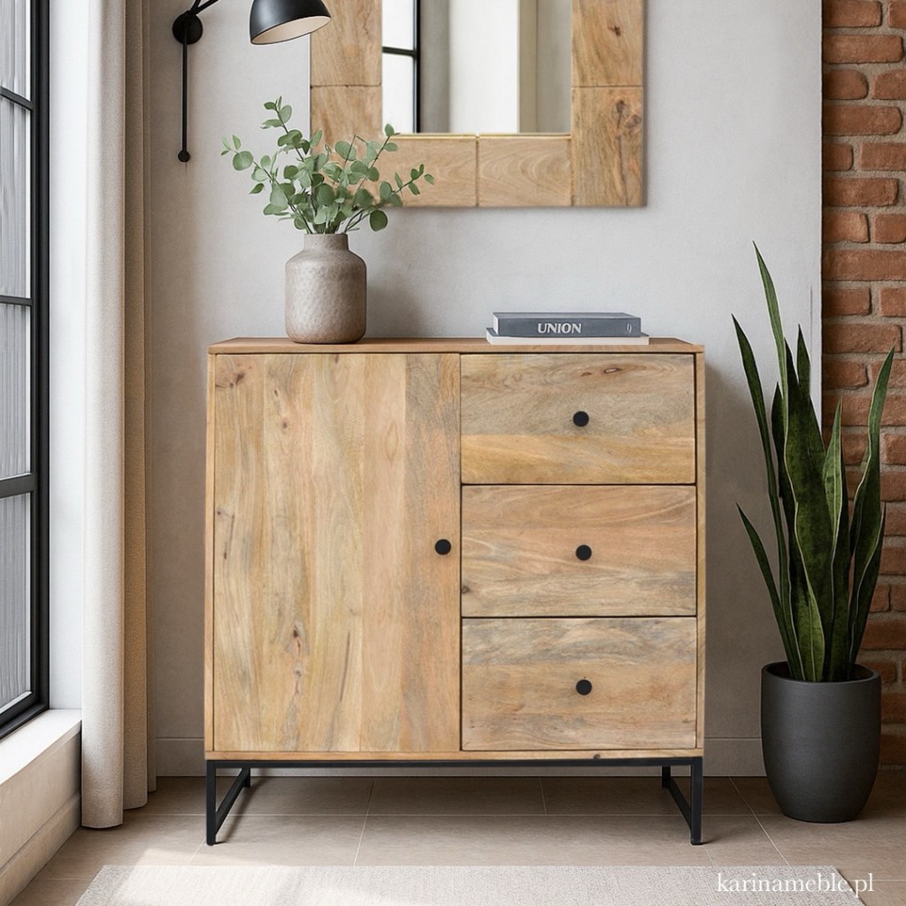 Minimalistyczna komoda z drewna mango z trzema szufladami i szafką, na czarnych metalowych nogach. Ustawiona w nowoczesnym, jasnym wnętrzu z rośliną i ozdobnym lustrem nad meblem. Produkt Karina Meble.
