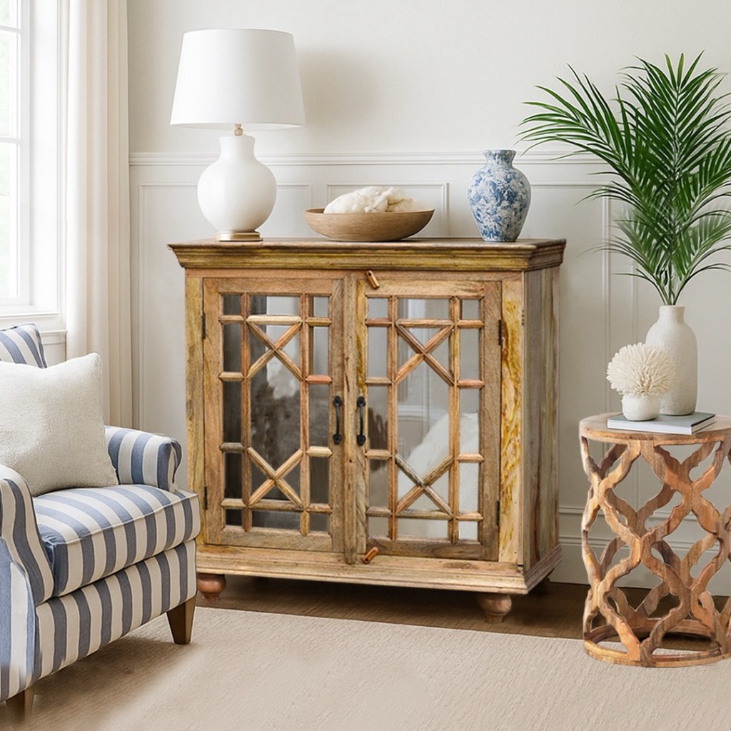 Drewniana komoda indyjska z lustrzanymi frontami i geometrycznym wzorem, ustawiona w jasnym wnętrzu w stylu boho i hampton, z roślinami i fotelami w pasy.